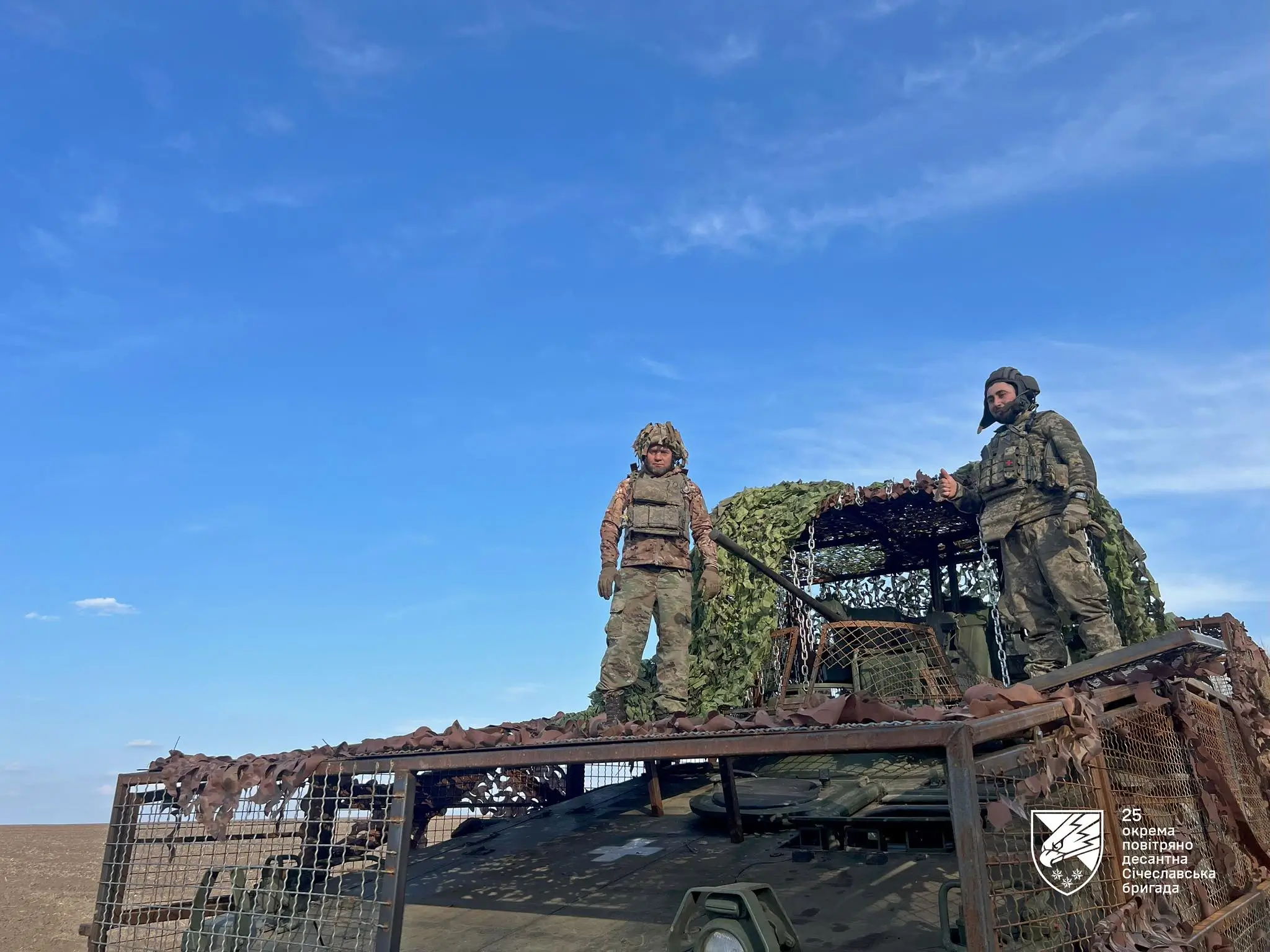 Two Ukrainian soldiers on a Marder 1A3 with a drone cage and grille protection.