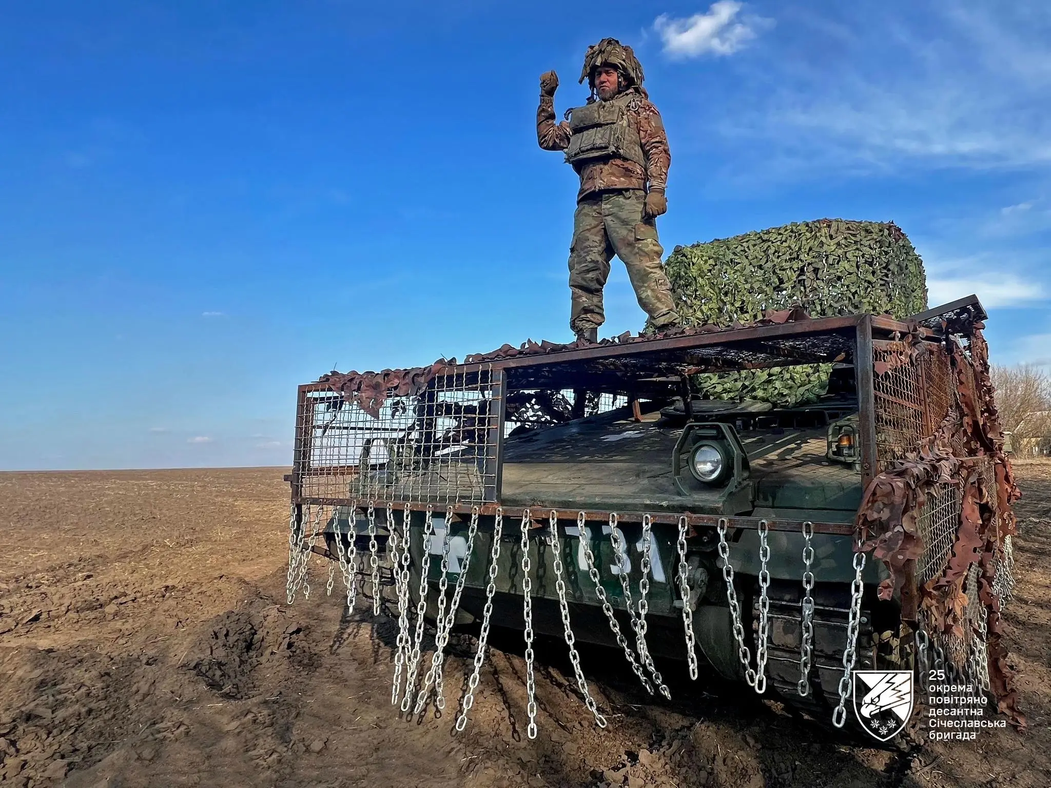 A Ukrainian soldier on a Marder 1A3 with a drone cage and chain+grille protection