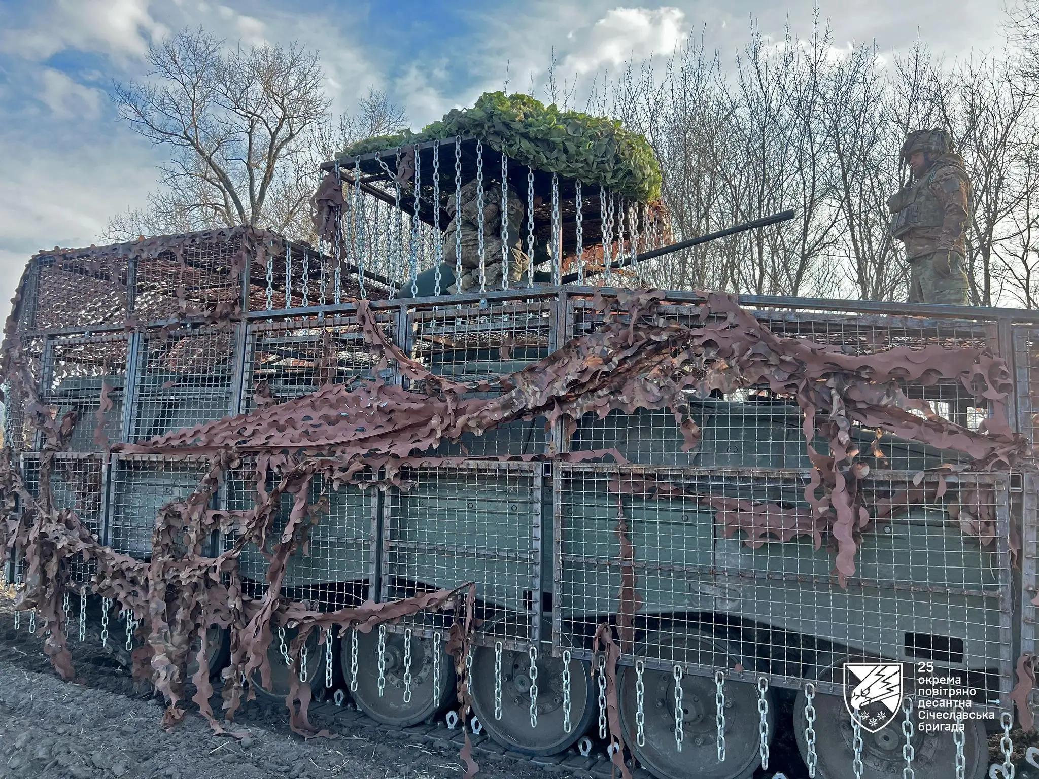 Two Ukrainian soldiers on a Marder 1A3 with a drone cage and chain+grille protection