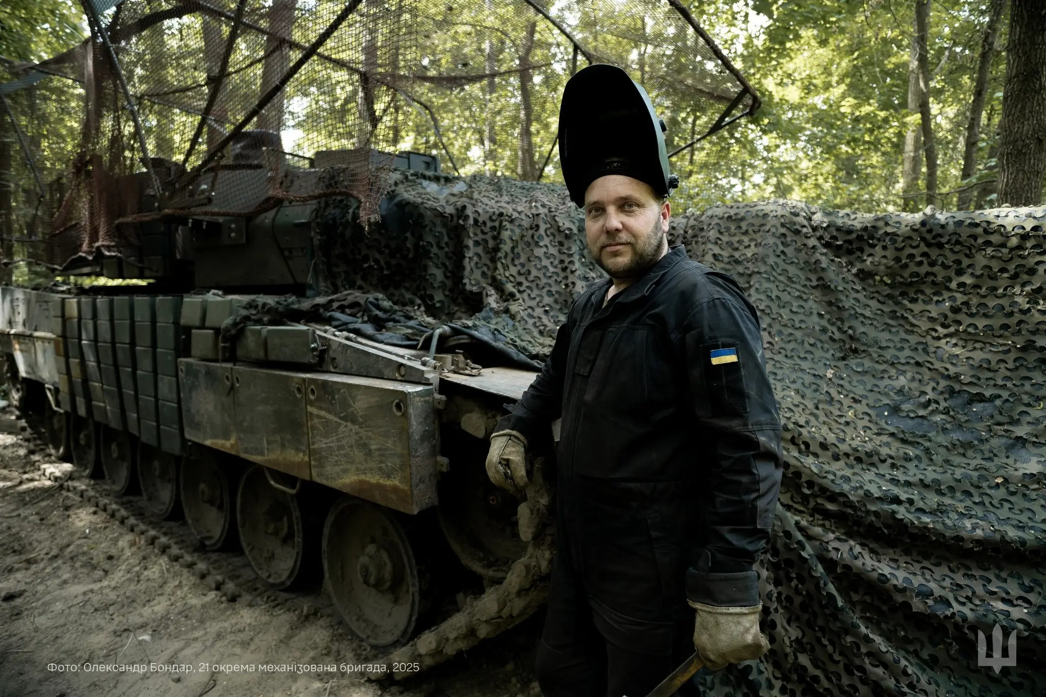 Ukrainian soldier standing in front of a Leopard 2A6 with grille protection, a drone cage and reactive armour somewhere in the Ukrainian woods